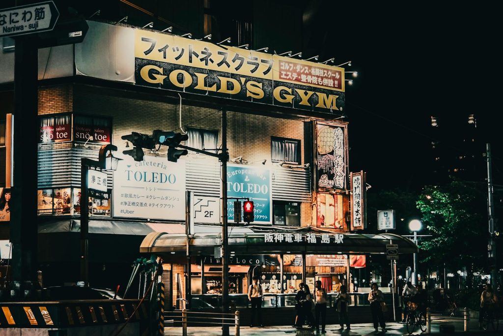Vibrant night scene of Gold's Gym and Cafeteria Toledo in Tokyo, Japan with city lights and signage.