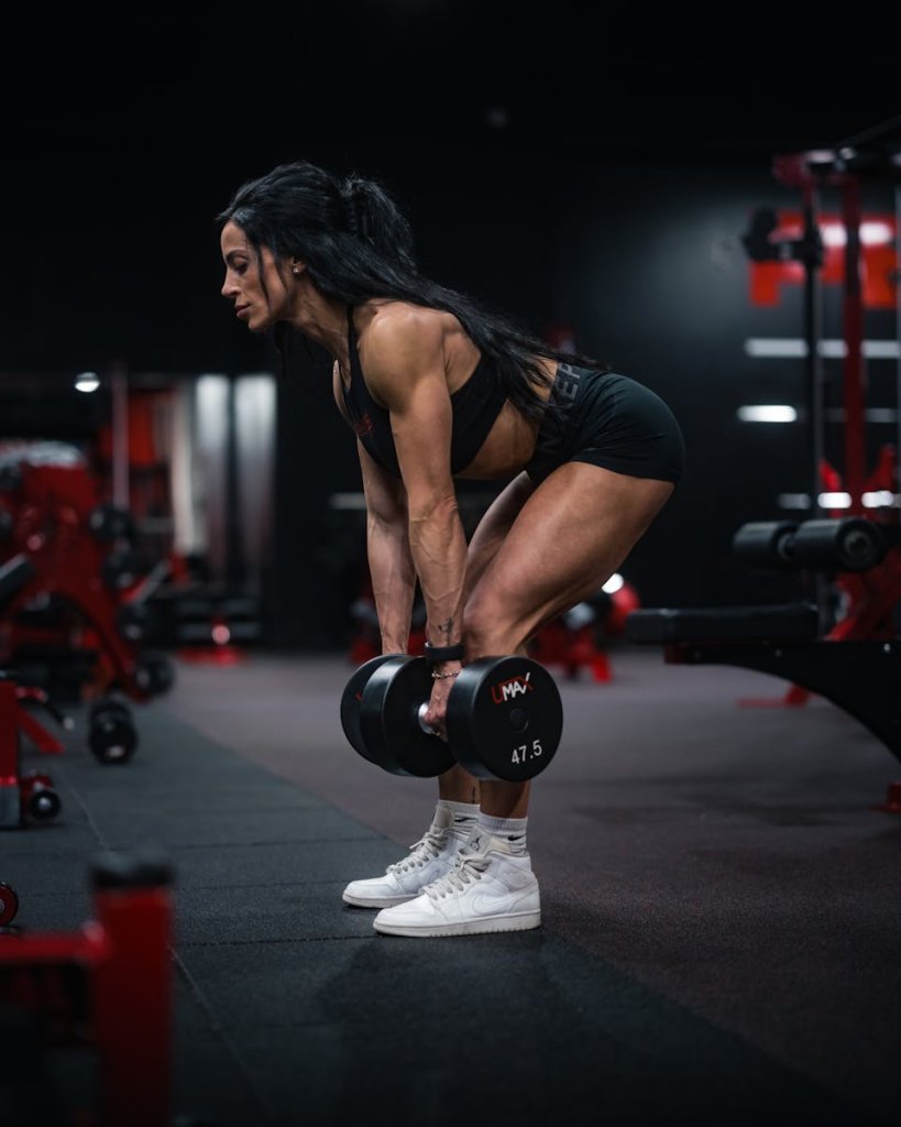 Strong female athlete lifting dumbbells in a gym setting, focused on strength training.