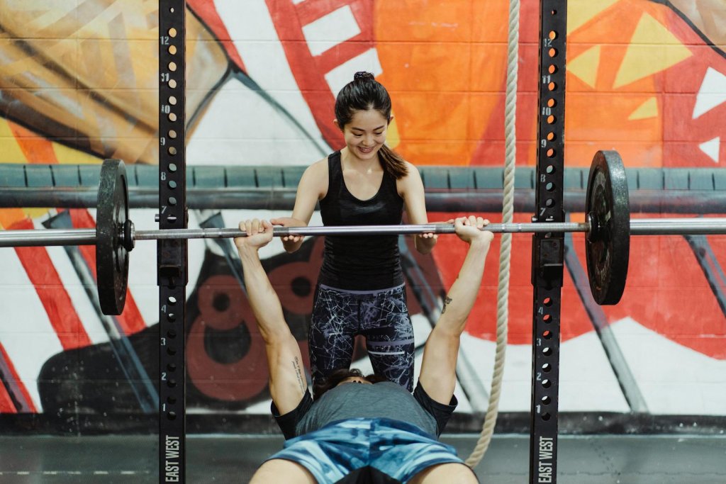 Asian couple engaged in fitness training at the gym, bench press exercise.