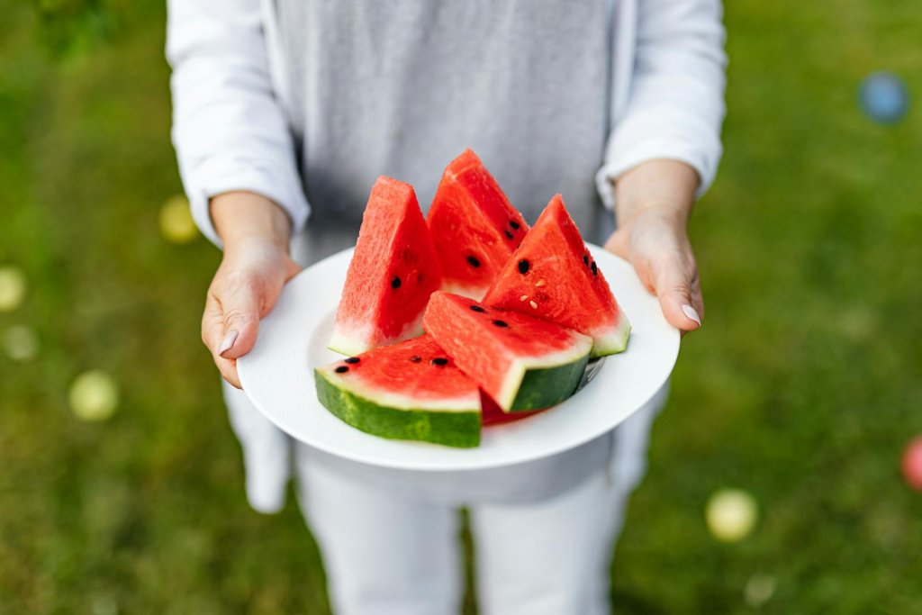 Hands holding a plate of juicy watermelon slices on a sunny day.