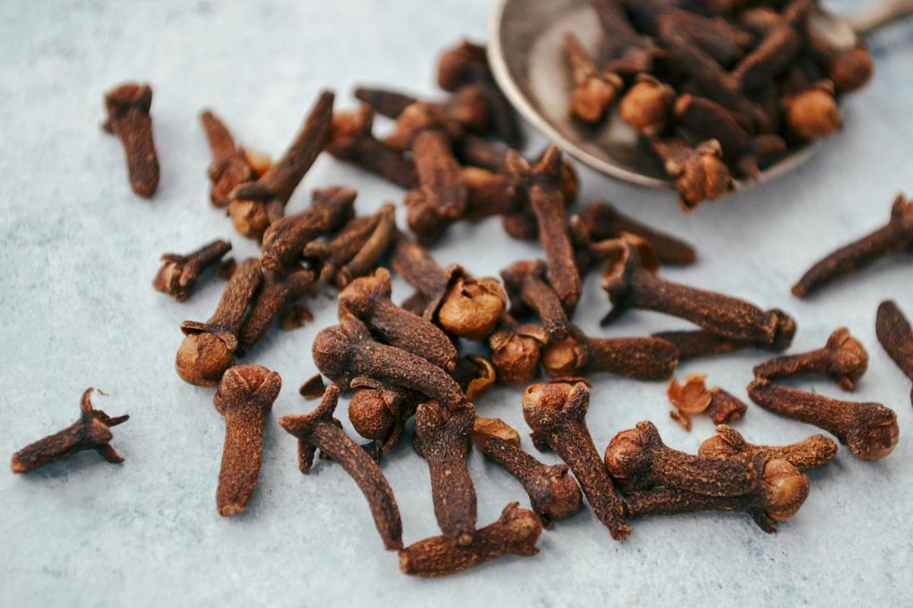 A close-up image of aromatic dry cloves scattered on a spoon over a gray surface.