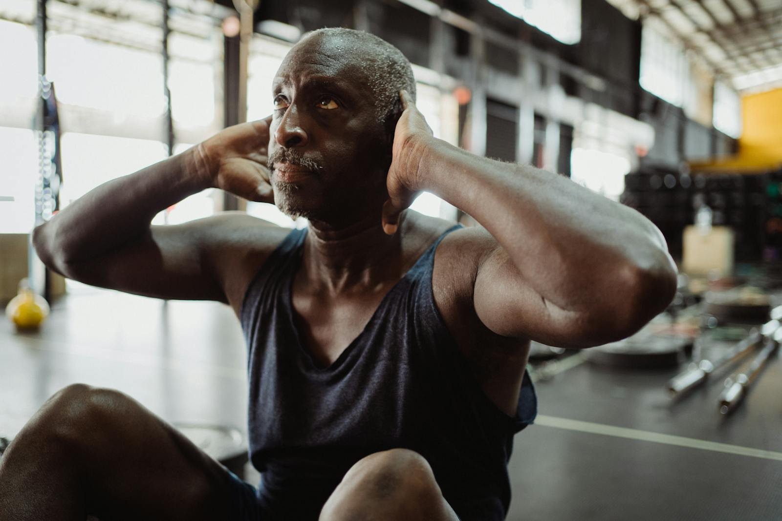 Mature man in tank top doing sit-ups in gym, focusing on strength and wellness.