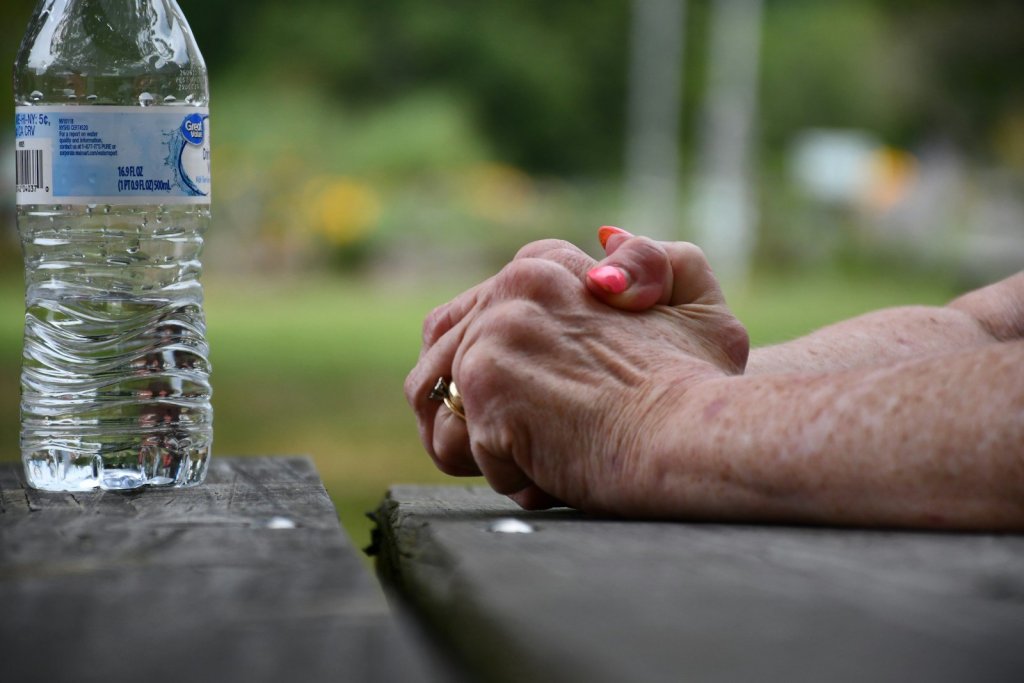 Hands clasped on a wooden picnic table near water bottle