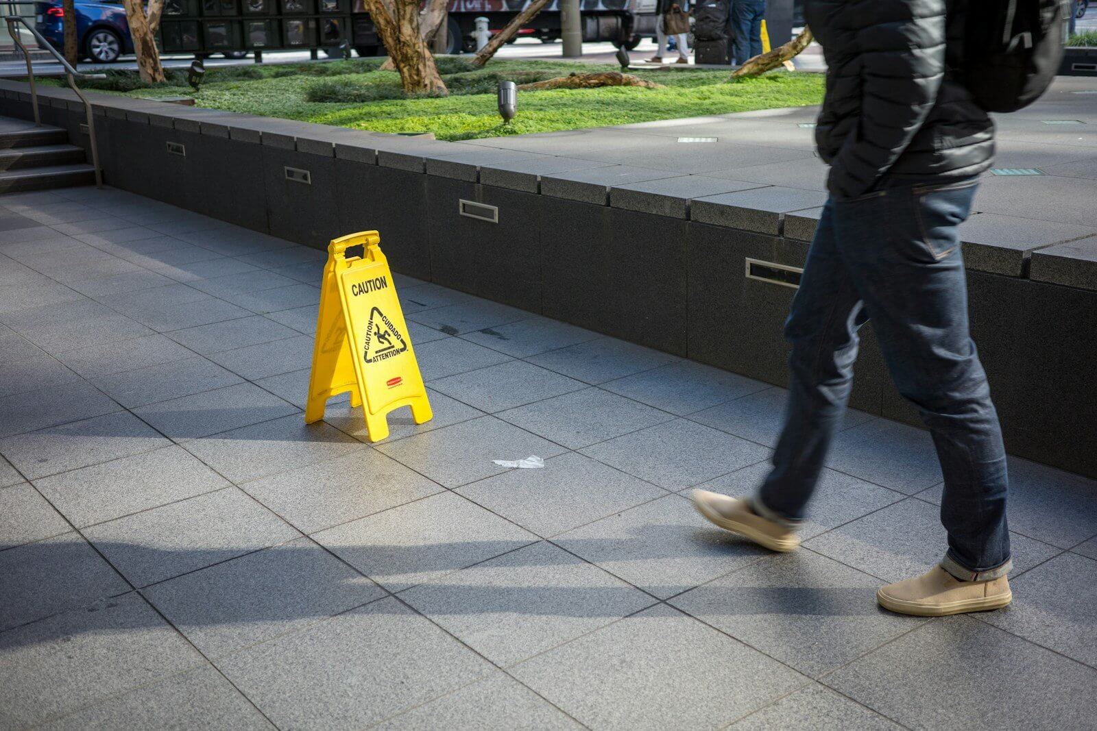 A man walking down a sidewalk next to a yellow caution sign